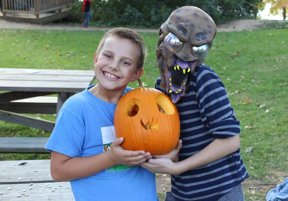 campers holding a carved pumpkin; one is wearing a Halloween mask